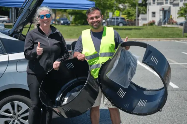 Woman in black outfit and man in neon vest hold compost bins at the Food Scraps to Soil event.
