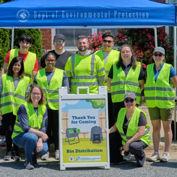 Volunteers in green vests stand in front of a blue tent during Montgomery County Department of Environmental Protection bin distribution event.
